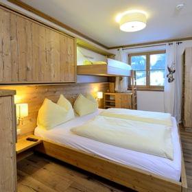Gemütliches Alpen-Hotelzimmer mit Holzmöbeln, Doppelbett, Etagenbett und Fenster mit Bergblick