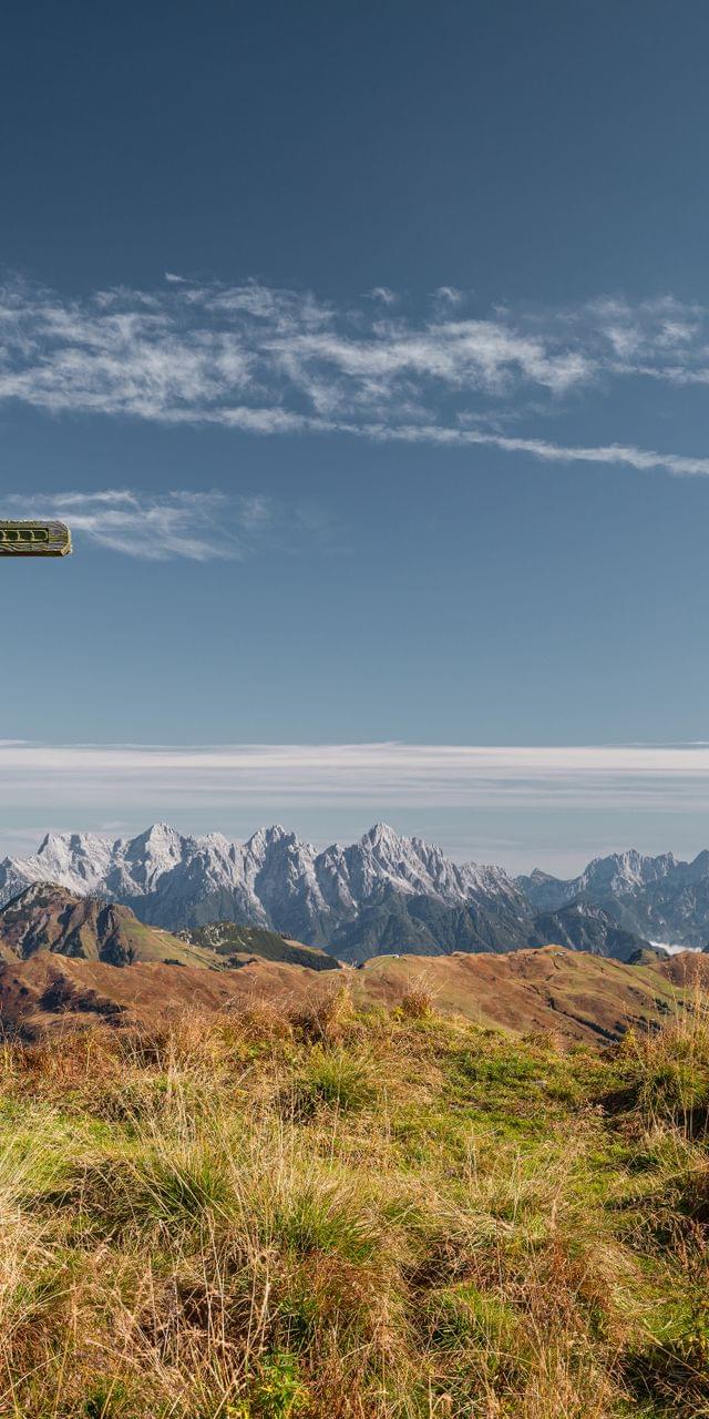 Gipfelkreuz auf Almwiese mit Panoramablick auf schneebedeckte Berggipfel