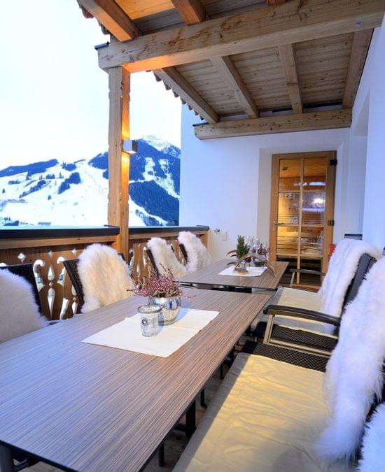 Gemütliche Alpenterrasse mit fellbedeckten Stühlen und Blick auf verschneite Berge