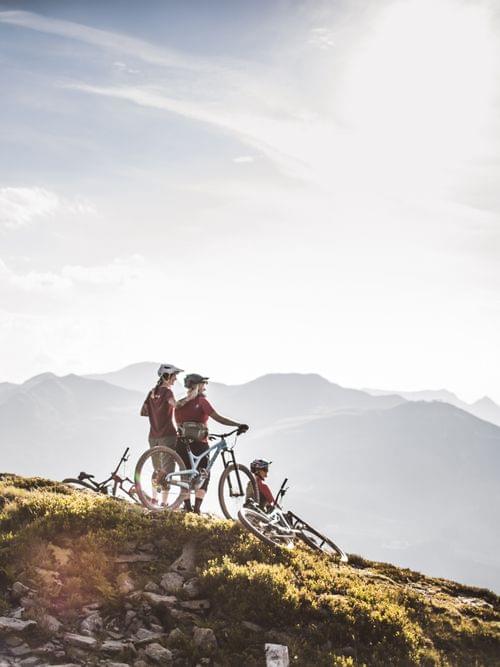 Radfahrer pausieren auf einem Bergpfad mit Alpenpanorama bei Sonnenuntergang