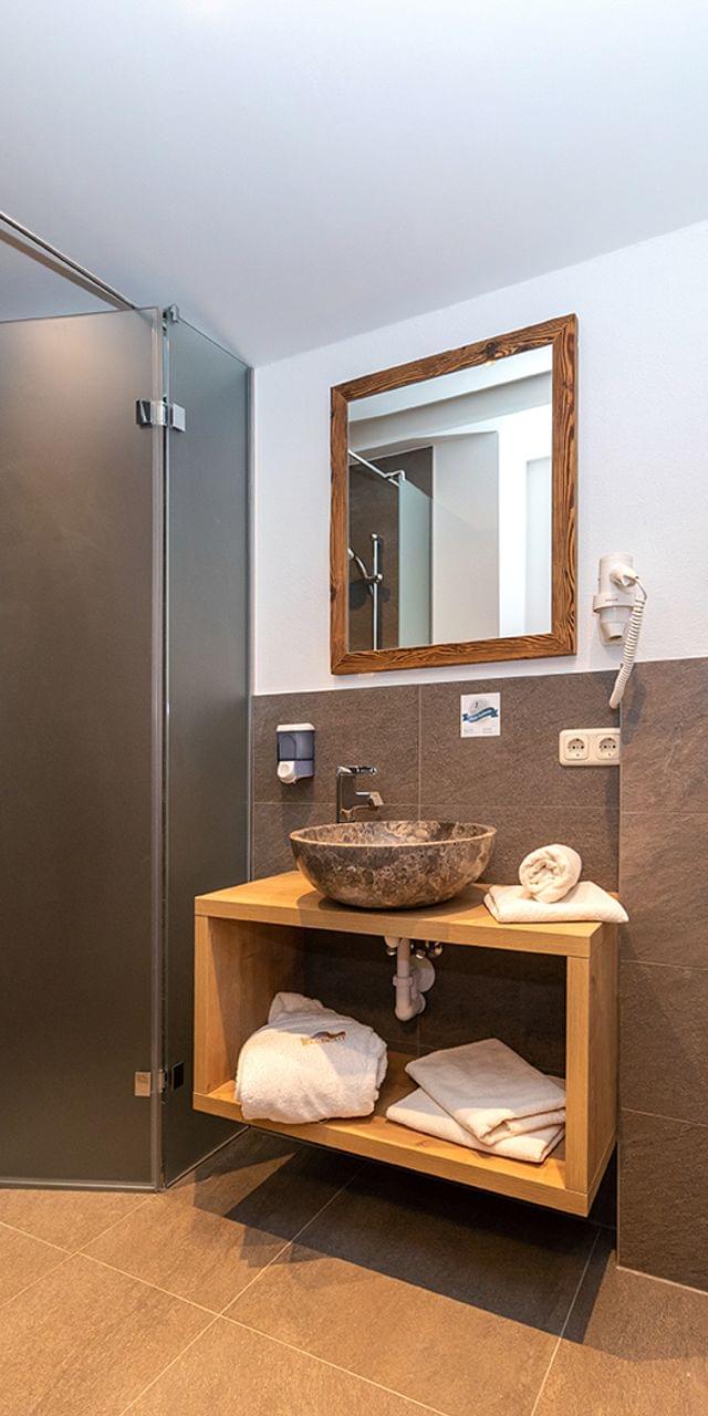 Modern hotel bathroom with walk-in shower, stone sink, wall-hung toilet and wooden vanity
