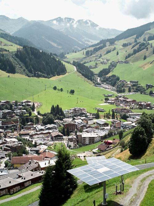 Alpendorf im grünen Tal mit Solarpaneelen und Skipisten im Hintergrund