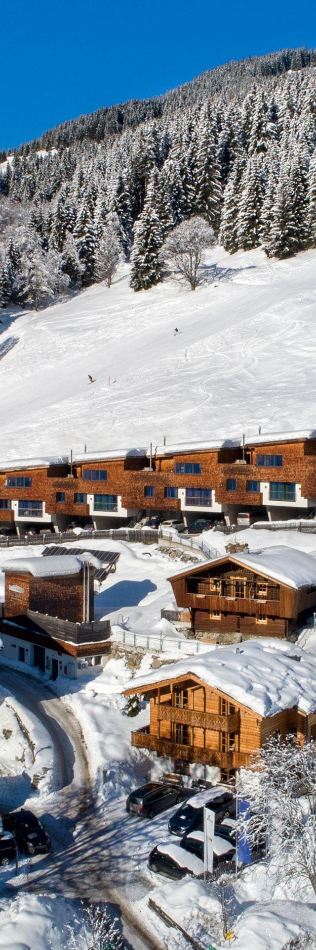 Snow-covered alpine village with modern chalets and ski slopes on a sunny winter day