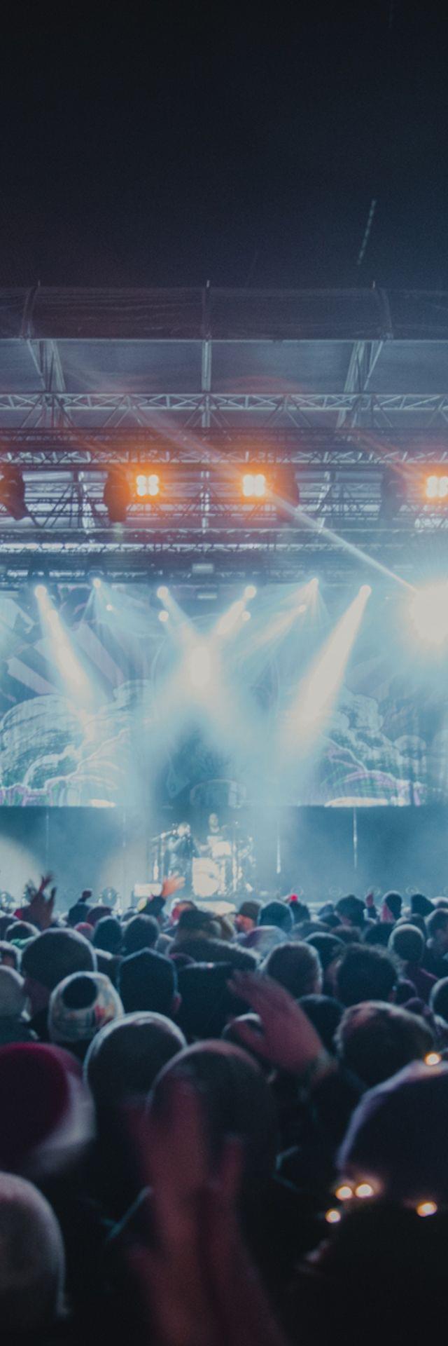Festival Veranstaltung, Bühne mit Licht und Band auf der Bühne, davor Besucher in Nachtstimmung 