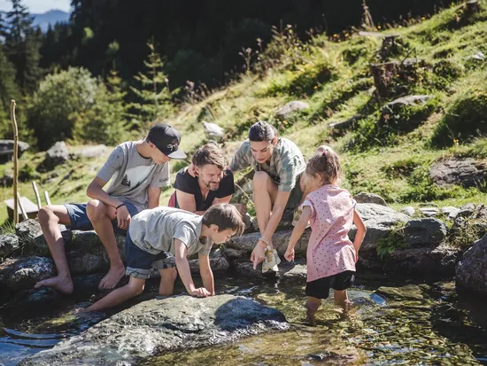 2 Erwachsene und 2 Kinder hocken am Wasser und genießen eine Abkühlung mitten in den Bergen 