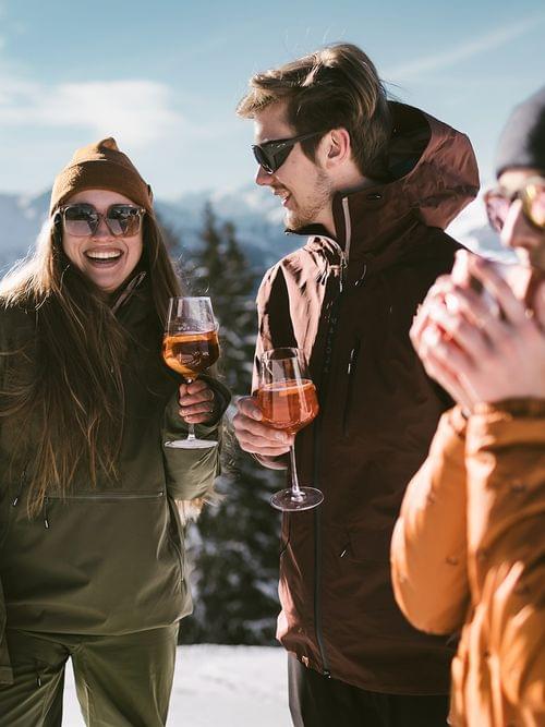 Freunde in Winterjacken genießen Getränke im Freien mit Blick auf verschneite Berge