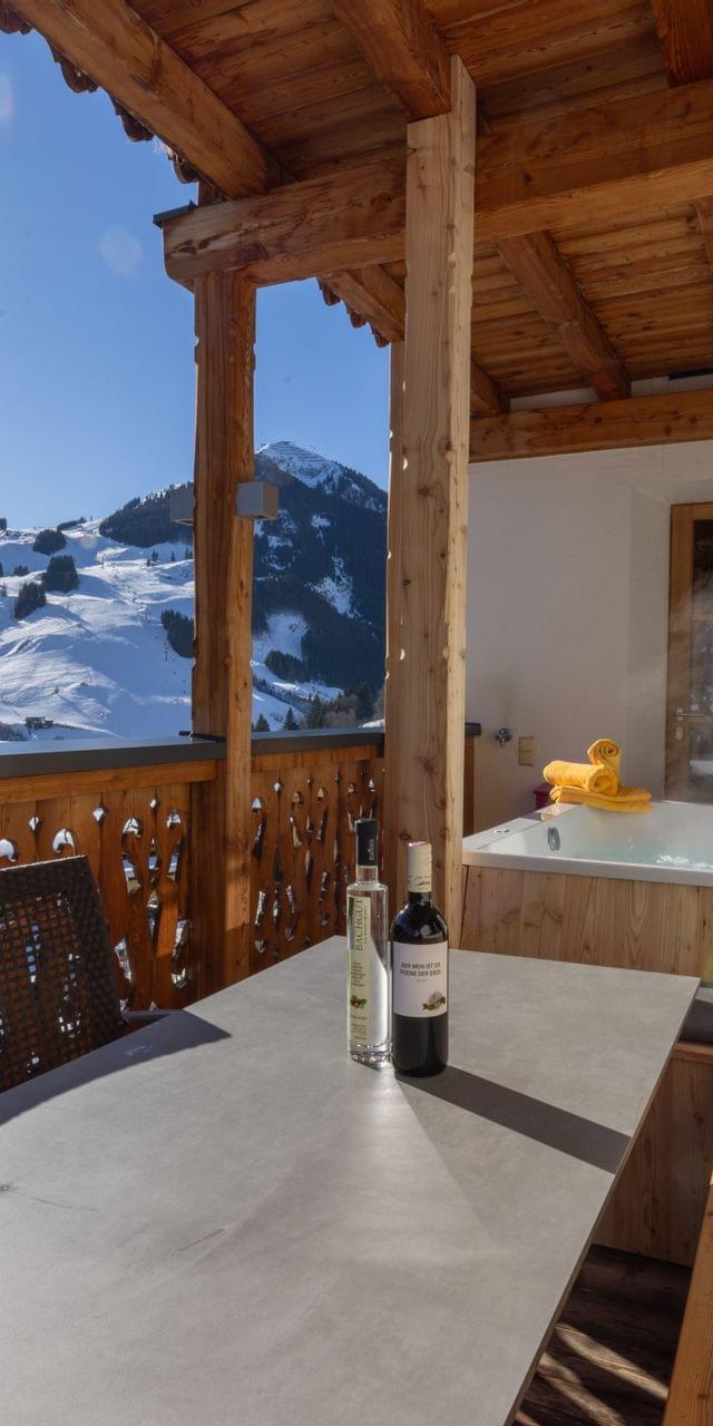 A view from the terrace of the main house suites overlooking the mountains of Saalbach Hinterglemm in winter, with a hot tub and a cozy seating area on the terrace.