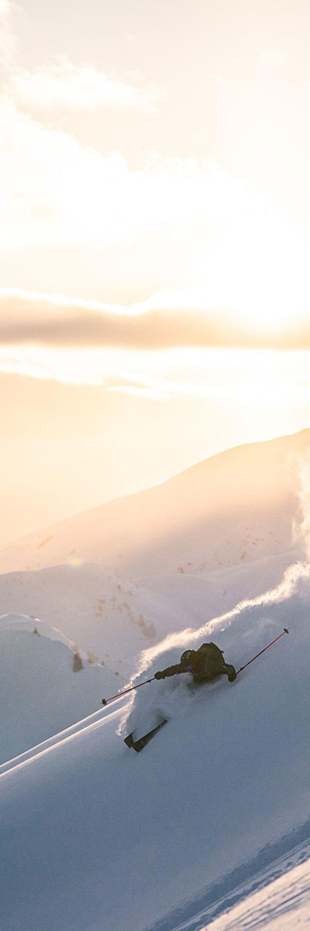 Skifahrer fährt durch frischen Pulverschnee an einem steilen Berghang bei Sonnenaufgang