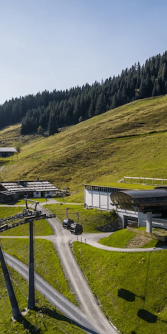 Bergbahnstation umgeben von grünen Hügeln und Wald im Sommer