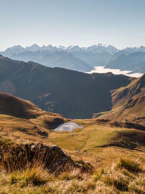 Alpine Landschaft mit grasbewachsenen Hängen, kleinem See und schneebedeckten Bergen im Hintergrund
