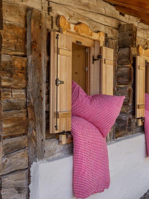 Red checkered bedding airing out of wooden alpine cabin windows