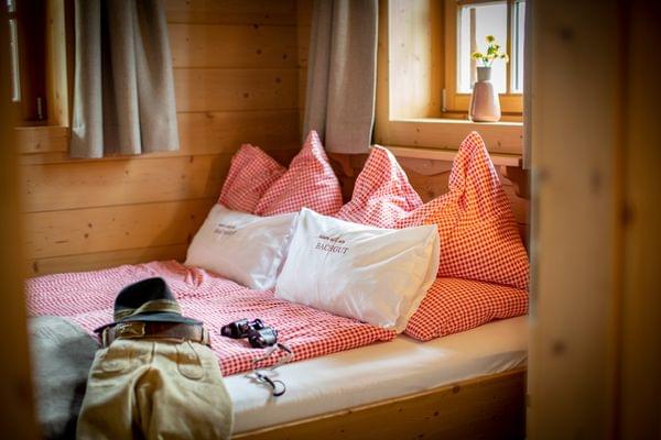 Gemütliches Alpenzimmer mit rotkariertem Bett, Wanderkleidung und Fernglas auf der Matratze