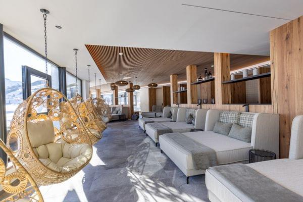 Badehaus Ruheraum mit Großen Liegen und Schwingsesseln vor Panorama-Fenster und Blick auf die verschneite Bergwelt 