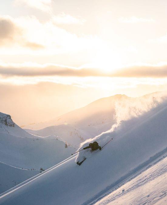 Skifahrer fährt durch frischen Pulverschnee an einem steilen Berghang bei Sonnenaufgang