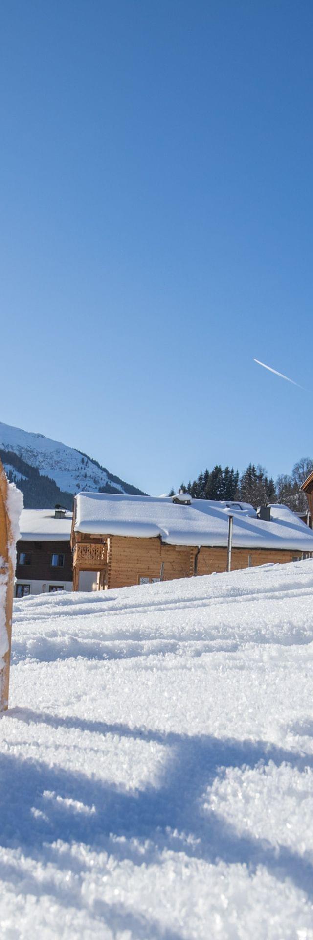 Holzschlitten auf verschneitem Hang mit Alpenchalets und sonniger Berglandschaft