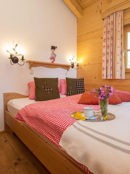 Cozy alpine bedroom with wooden furniture, red gingham bedding, and a tray with coffee and flowers
