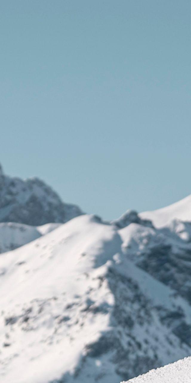 Drei Frauen in Skikleidung geben sich High-Five auf verschneiter Piste mit Berggipfeln im Hintergrund