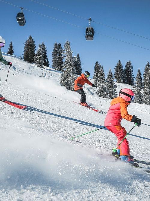 Familie fährt an einem sonnigen Wintertag im alpinen Skigebiet den Hang hinunter