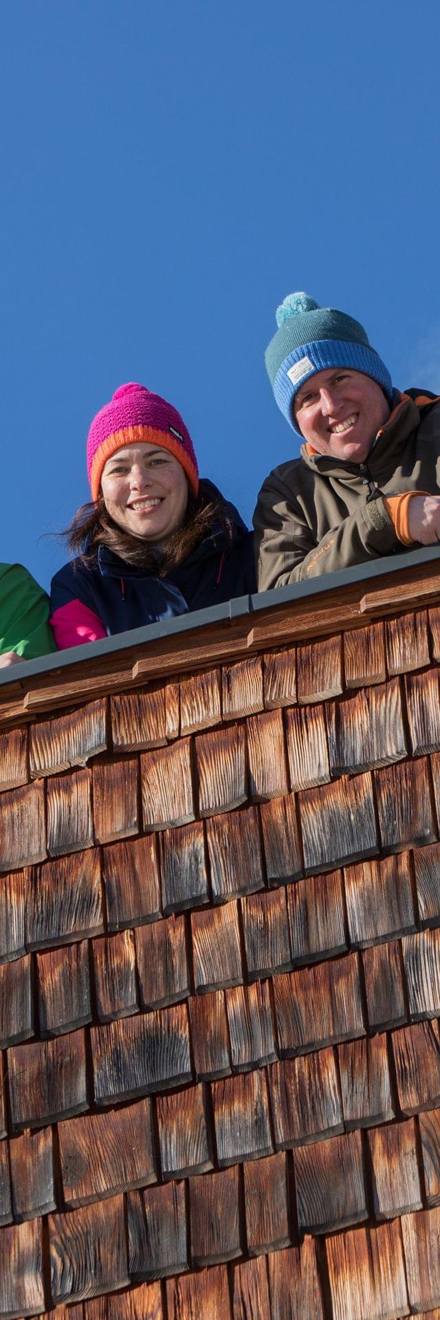 Group of smiling friends in winter clothes leaning over snowy cabin balcony