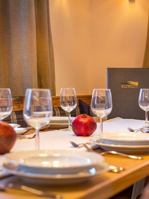 Cozy restaurant table set with plates, wine glasses, pomegranates, and menu at Bachgut