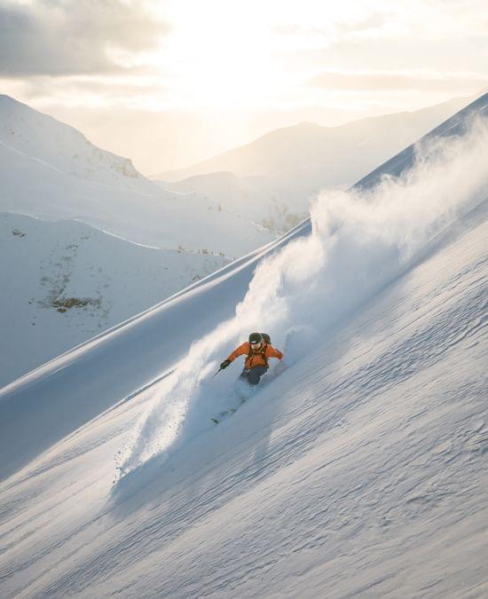 Skier in orange jacket carving through deep powder on a sunny mountain slope
