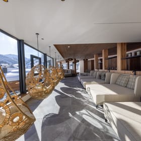 A relaxation room with large loungers and hanging chairs, overlooking the snow-covered mountain landscape.