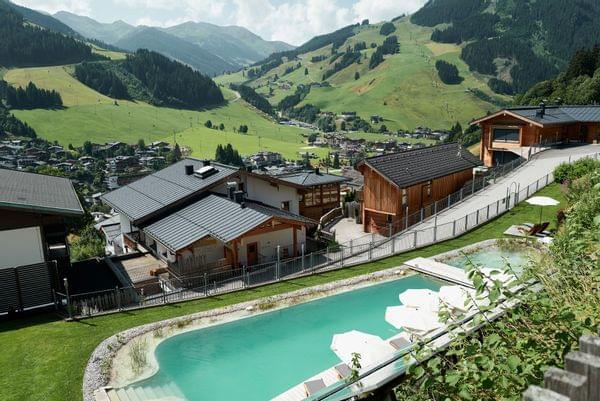 Luxury alpine resort with pool and wooden chalets overlooking mountain valley in summer