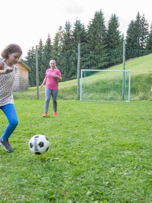 Kinder spielen Fußball auf einer Wiese in den Bergen, während Eltern in der Nähe zuschauen