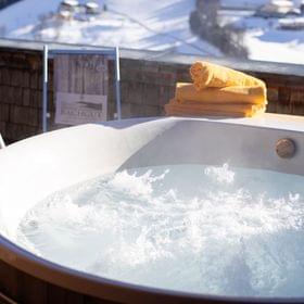 A bubbling hot tub on the terrace with lounge chairs, with a snowy winter landscape in the background.