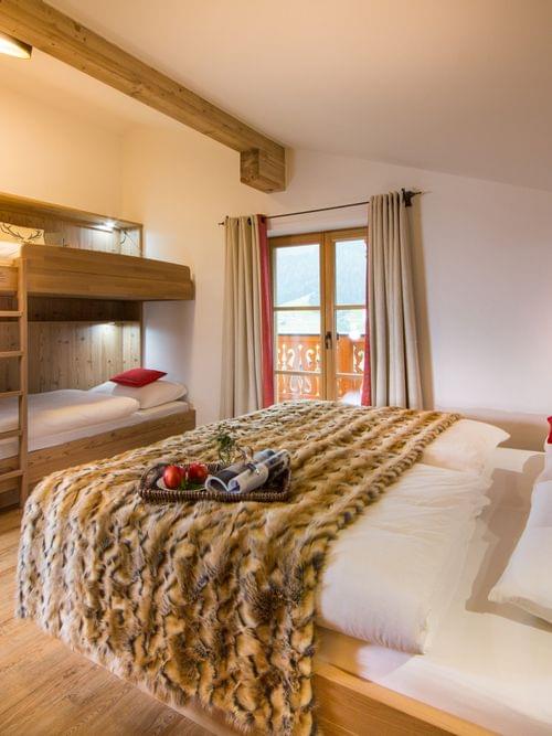 Cozy alpine hotel room with double bed, bunk beds, wooden decor and mountain view