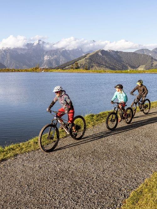 Family cycling along a lake path with mountain views in the background