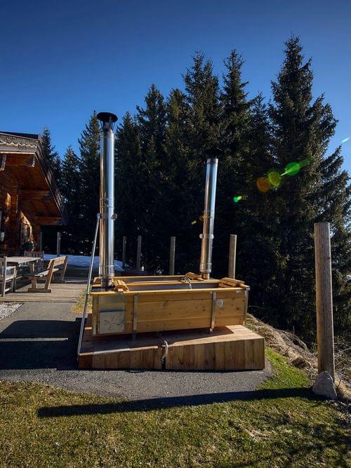 Bachalm Außenansicht im Ski-Frühling, 2 Außenbadewannen die mit Holz beheizt werden stehen im Hintergrund 