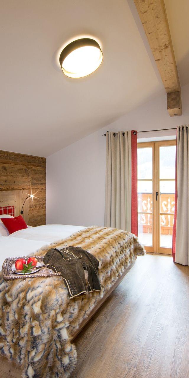 Gemütliches Alpenhotelzimmer mit Holzmöbeln, Doppelbett, Kunstfelldecke und Balkonblick