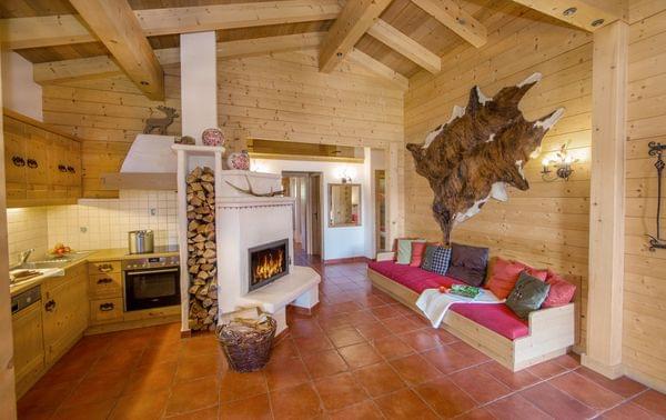 Cozy chalet interior with wooden walls, fireplace, open kitchen and built-in sofa with colorful pillows