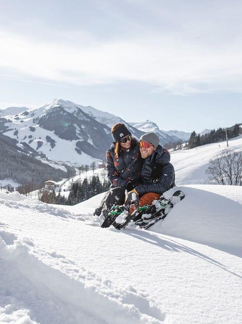 Couple sitting in the snow with skis, enjoying a sunny winter day in the mountains