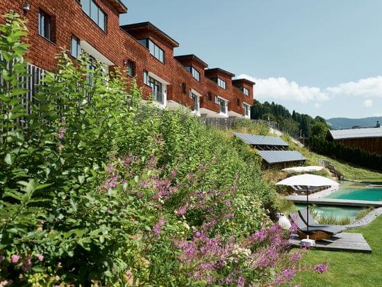 Umweltfreundliches Hotel mit Holzfassade, Naturpool, Solarpanels und üppigem Garten in Alpenlandschaft