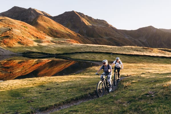 Two mountain bikers riding along a trail on the mountain, with an autumn landscape.