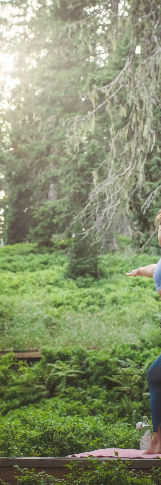 2 Frauen die im Wald auf einer Plattform Yoga machen 