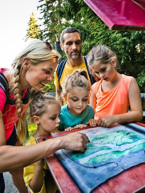 Familie mit Kindern liest im Sommer eine Wanderkarte im Wald