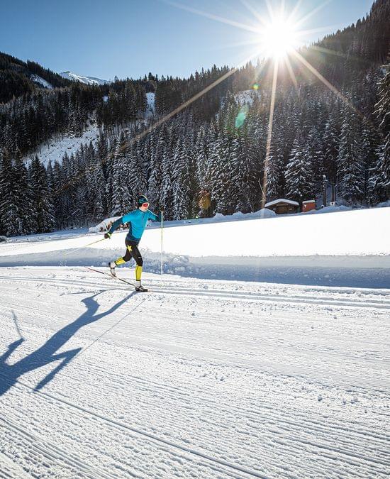 Cross-country skier gliding on groomed snowy trail in mountain landscape under bright sun