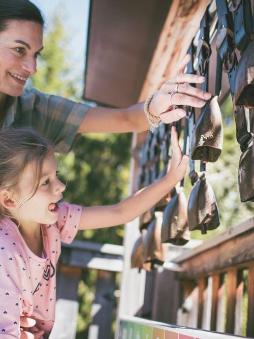 Mother and daughter playing with hanging cowbells at outdoor nature park