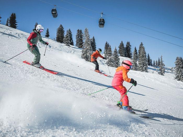 Family skiing downhill on a sunny winter day in alpine ski resort with snowy trees
