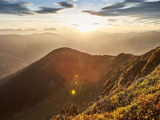 Sonnenaufgang über Gebirgskamm mit nebligen Tälern und dramatischem Himmel in den Alpen