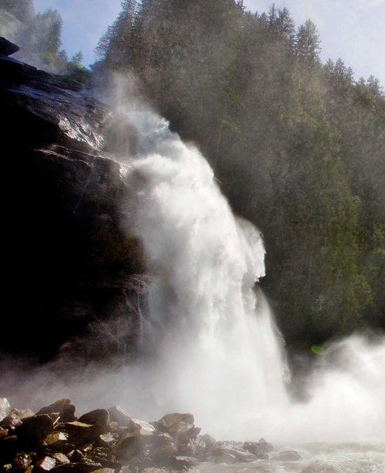 Person steht auf moosigen Felsen nahe kraftvollem Wasserfall im nebligen Bergwald