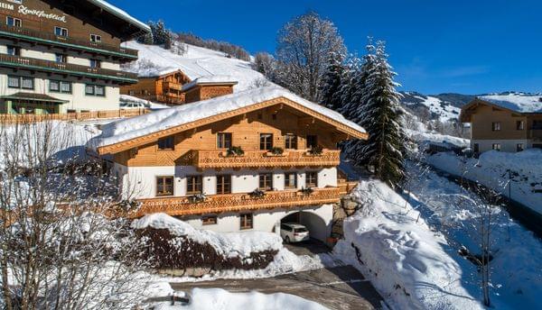 Traditionelles Alpenchalet im verschneiten Bergdorf unter klarem blauen Himmel