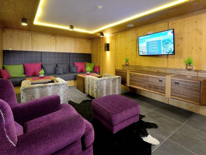 Gemütliche Alpenlounge mit lila Sesseln, fellbezogenen Hockern und Wandfernseher