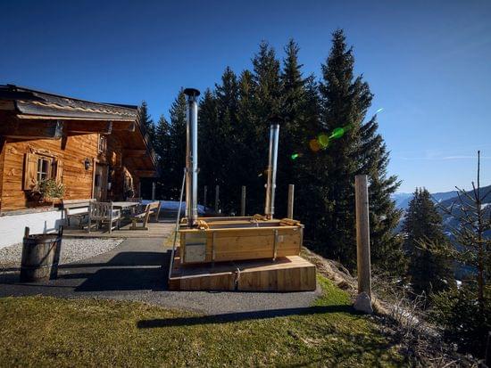 Bachalm Außenansicht im Ski-Frühling, 2 Außenbadewannen die mit Holz beheizt werden stehen im Hintergrund 