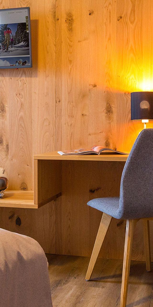 Cozy hotel room with wooden wall, flat-screen TV, ski gear, and desk with reading lamp