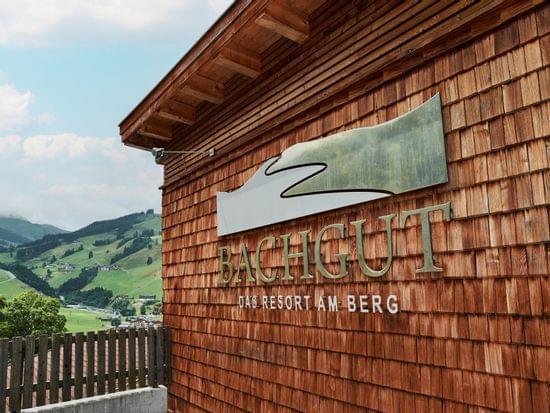 Bachgut Resortschild an Holzfassade mit Blick auf ein alpines Tal im Hintergrund