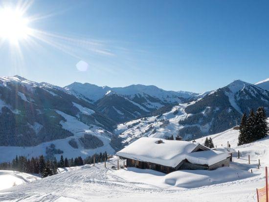Bachalm Außenansicht im Winter, Berge in Schnee gehüllt und Sonnenschein 